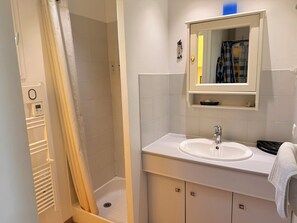 Een badkamer met een douche, wastafel en spiegel.