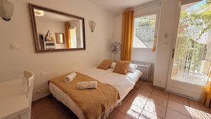 Quarto com cama, ventoinha, aquecedor e janela com cortinas.
