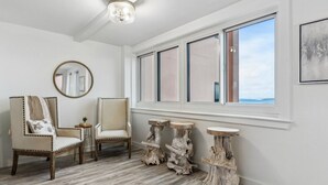 Ein Zimmer mit großem Fenster, zwei Stühlen, einem runden Spiegel und drei rustikalen Holztischen.