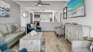 Ein modernes Wohnzimmer mit einem grauen Sofa, blauen Sesseln, einem Couchtisch und einer Küche im Hintergrund.