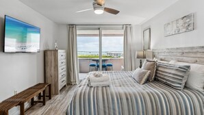 Ein modernes Hotelzimmer mit einem großen Bett, einem Deckenventilator, einem Fernseher, einem Balkon mit Blick und einer hölzernen Bank.