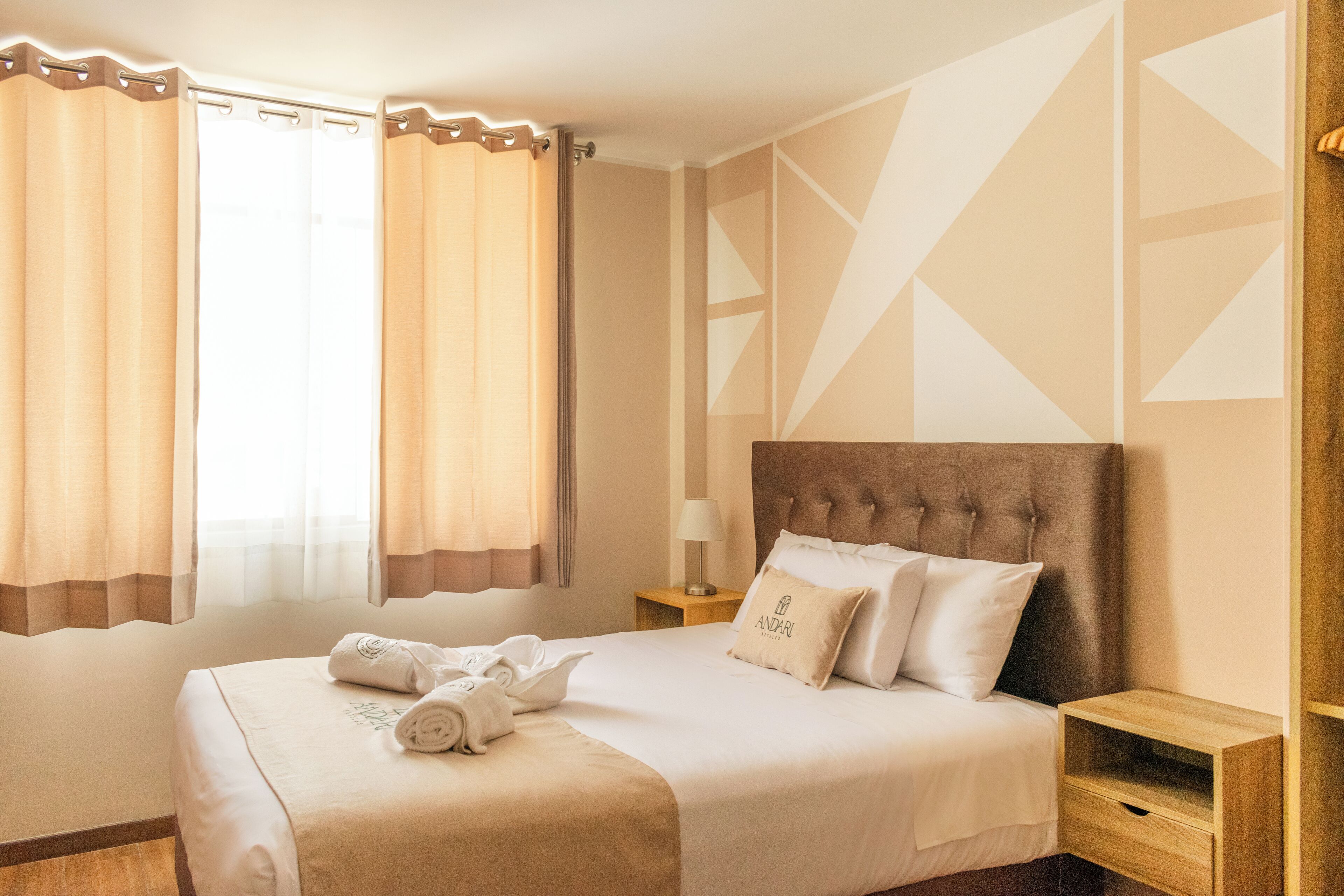 A hotel room with a large bed, a nightstand, a lamp, and a window with curtains.