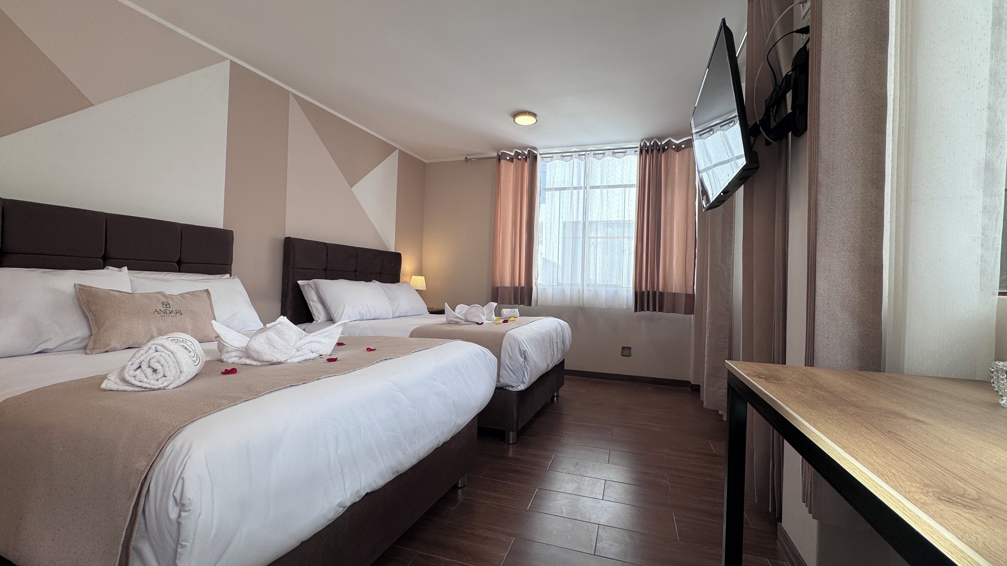 Habitación de hotel con dos camas, un escritorio, un televisor y una ventana con cortinas.