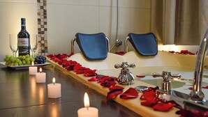 A bathroom with a bathtub, two blue chairs, a bottle of wine, and candles. - ANDARI HOTELES (Arequipa)