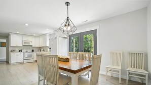 Una cocina moderna con armarios blancos, una mesa de comedor de madera y una lámpara colgante geométrica original.