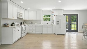 Una cucina moderna con mobili bianchi, forno ventilato, microonde e lavastoviglie. Si nota una finestra sopra il lavello e una porta che dà all'esterno.