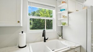 Una cucina moderna con un piano di lavoro bianco, un lavello e una finestra vista su un paesaggio verde.