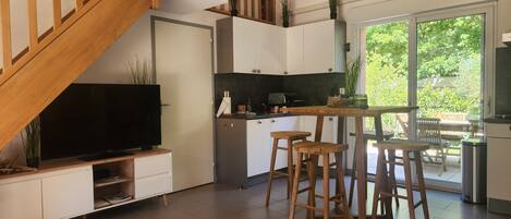 Una cocina moderna con comedor, escalera de madera y un amplio ventanal con vistas al verdor.