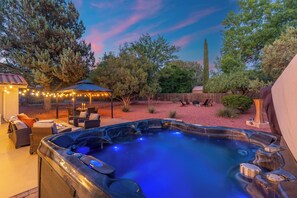 A hot tub surrounded by outdoor furniture, a pergola with string lights, and a wooden fence. - Vysta Bonita: Views, Cold Plunge, Hot Tub, Firepits, Trails, Near Chapel (Sedona)