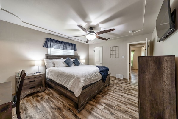 A bedroom with a wooden bed, a ceiling fan, a nightstand, and a desk.