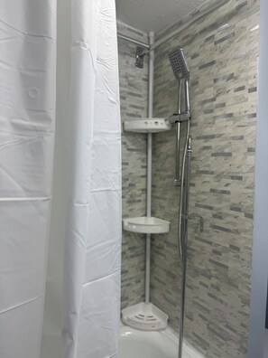 A shower area with a handheld showerhead, a wall-mounted faucet, and a small white shelf.