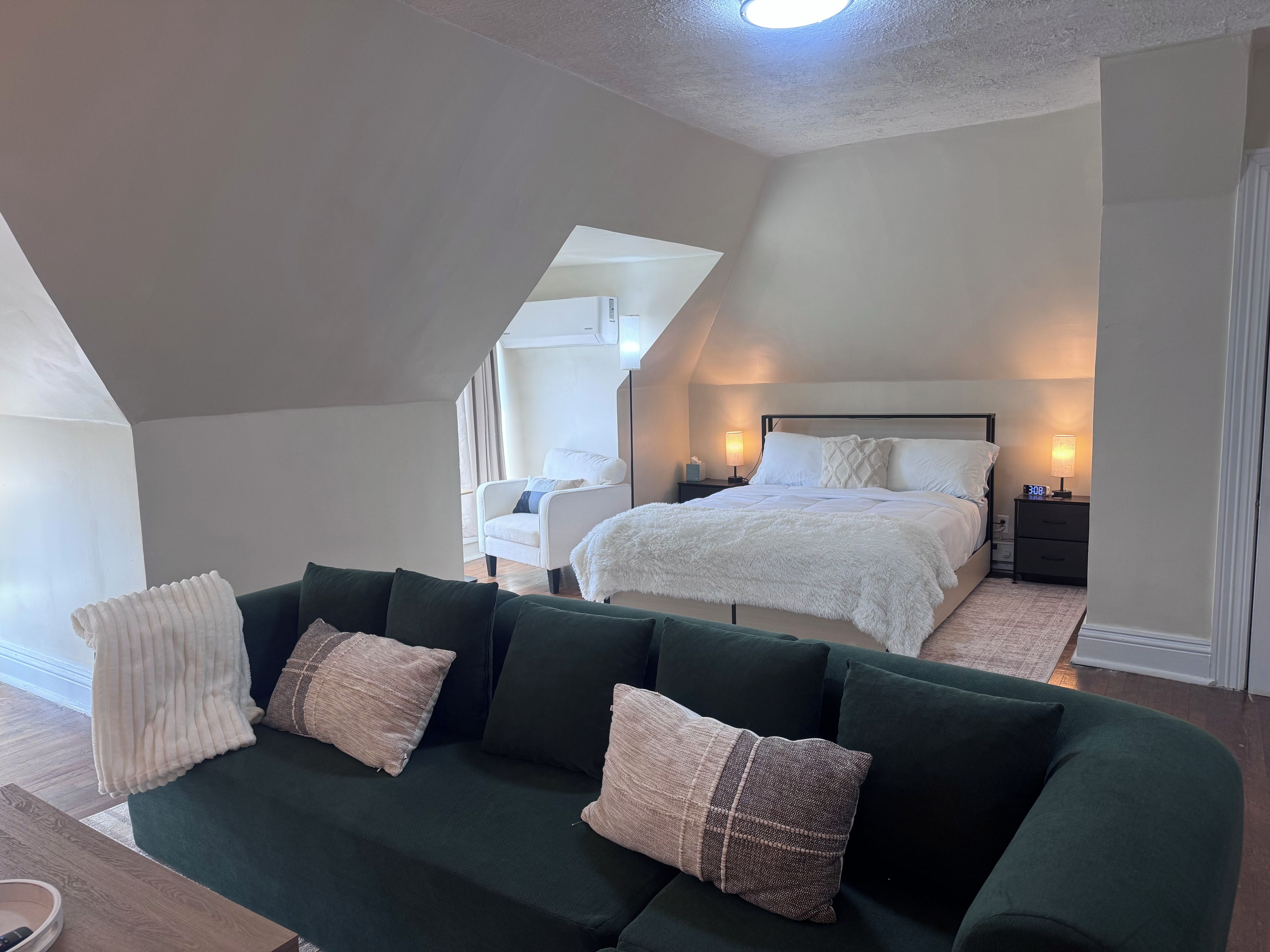 Un dormitorio moderno con una cama grande, un sofá verde y una mesita de noche con una lámpara.
