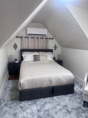 A bedroom with a bed, nightstands, an air conditioning unit, and a fluffy rug.