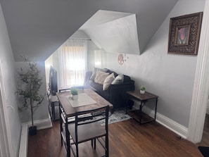 A cozy living room with a dining area, a sofa, a small table, and a potted plant.