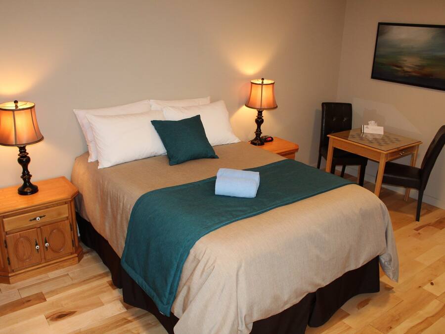 A neatly arranged bedroom with a bed, two bedside tables with lamps, a chair, and a small table with a tissue box.