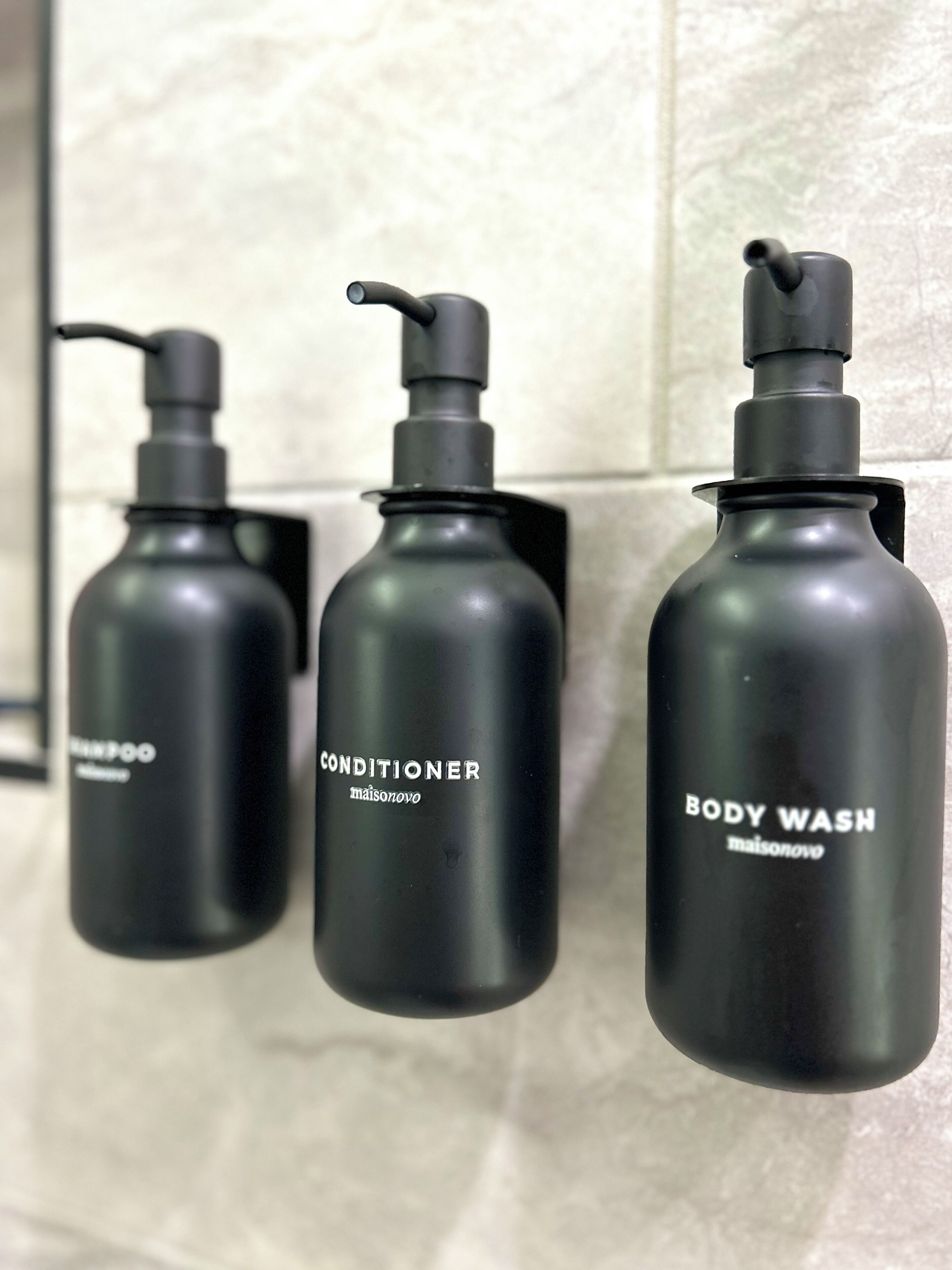 Three black bottles of toiletries on a tiled wall.