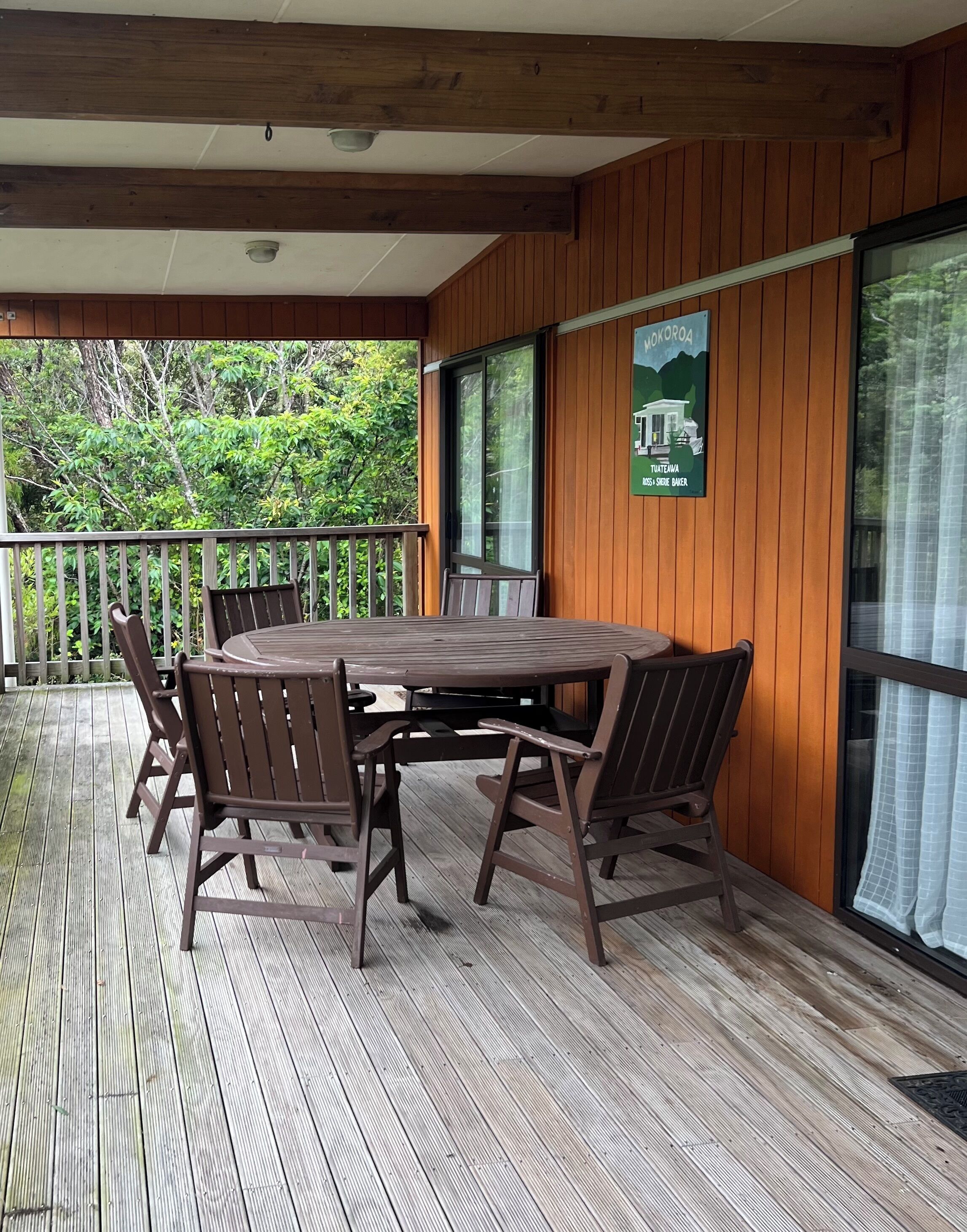 Un espacio al aire libre techado con una mesa y sillas de madera, un cartel que indica un lugar en Guatemala y vistas de follaje.