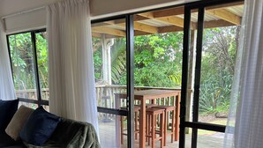 Una habitación con un amplio ventanal corredera que da a una terraza exterior, una mesa de madera y un sofá con cojines.