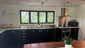 Una cocina moderna con armarios oscuros, electrodomésticos de acero inoxidable y un amplio ventanal con vistas a árboles.