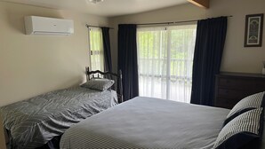 Un dormitorio con dos camas individuales, un ventilador de techo, un equipo de aire acondicionado y una ventana con cortinas.