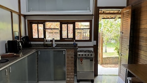 A modern kitchen with a built-in oven, a coffee machine, and a dining area with a wooden table and chairs. - Pousada Villa Itohã (Prado)