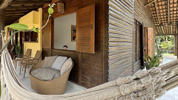 A hammock chair in a covered outdoor area with a wooden ceiling and a view of the outside. - Pousada Villa Itohã (Prado)