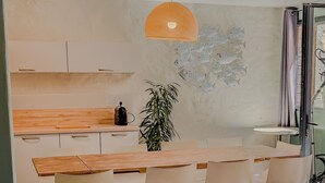 A modern dining area with a wooden table, white chairs, and a wicker chair with a cushion.