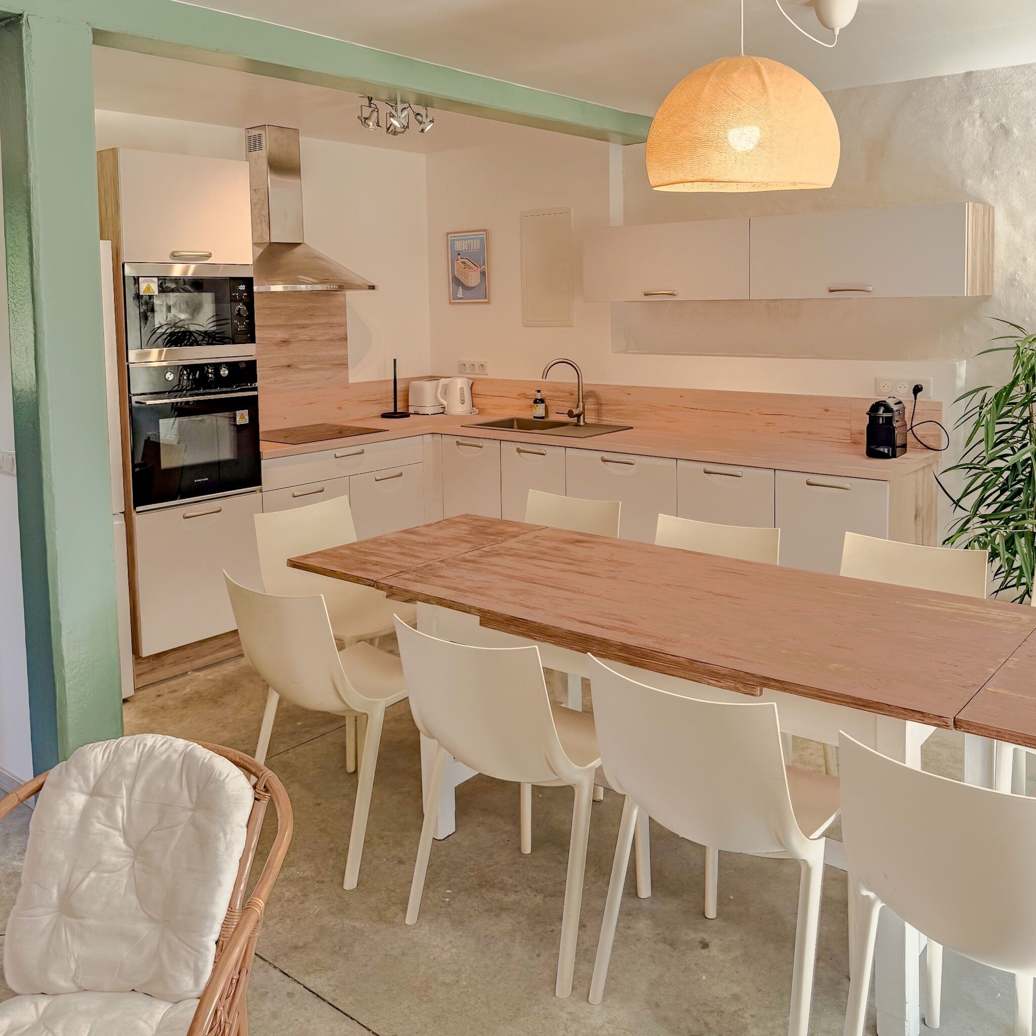 A modern kitchen with a wooden countertop, white chairs, and a hanging light fixture.