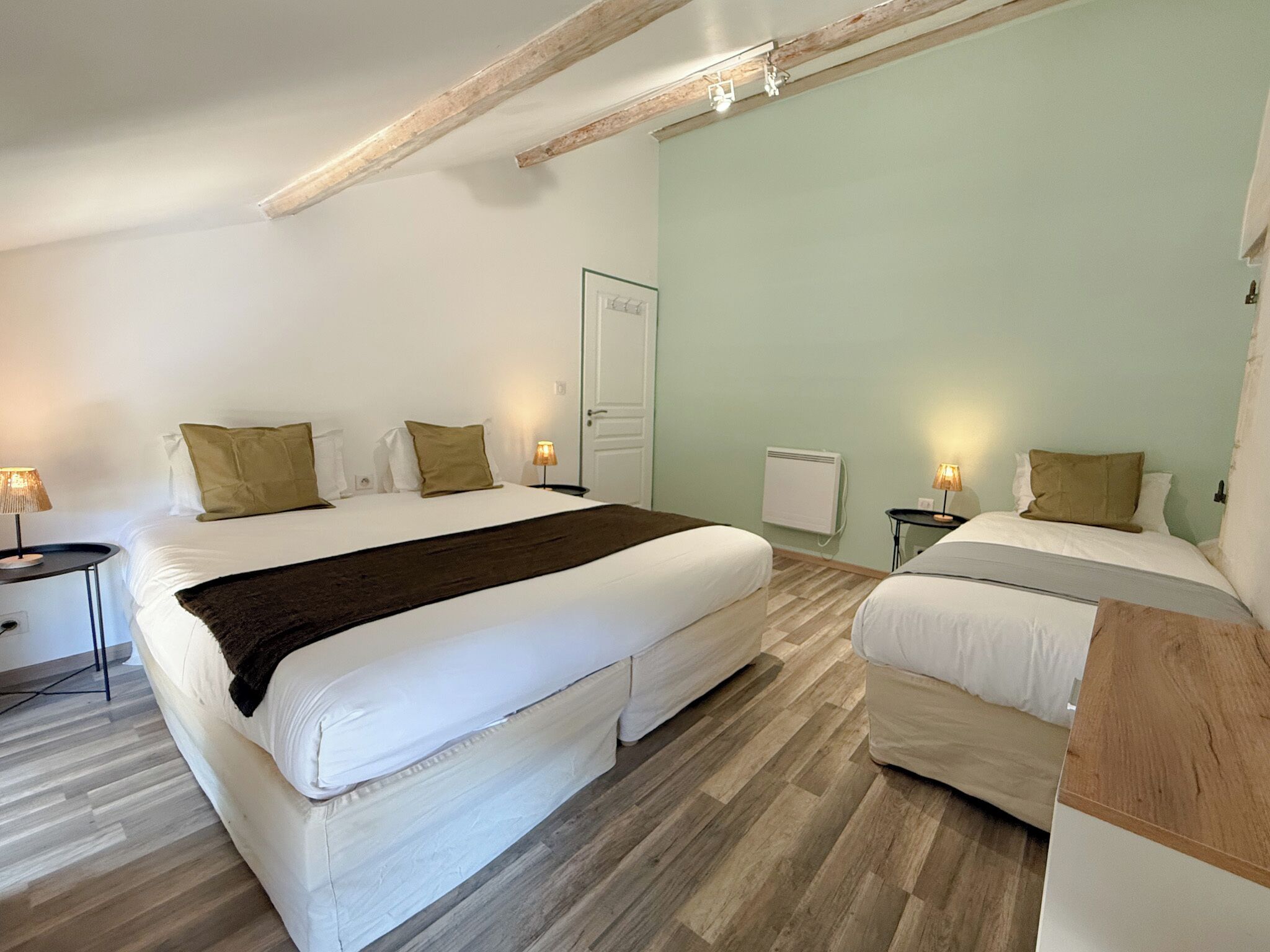 A bedroom with two beds, a wooden floor, and a white door.