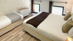 A bedroom with a large bed, a smaller bed, a nightstand, a lamp, and a window with curtains.