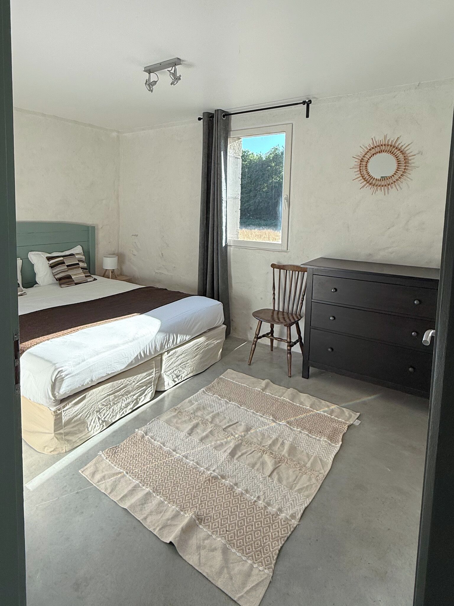 Un dormitorio con dos camas, un tocador, una silla, un ventanal y una decoración de sol en la pared.