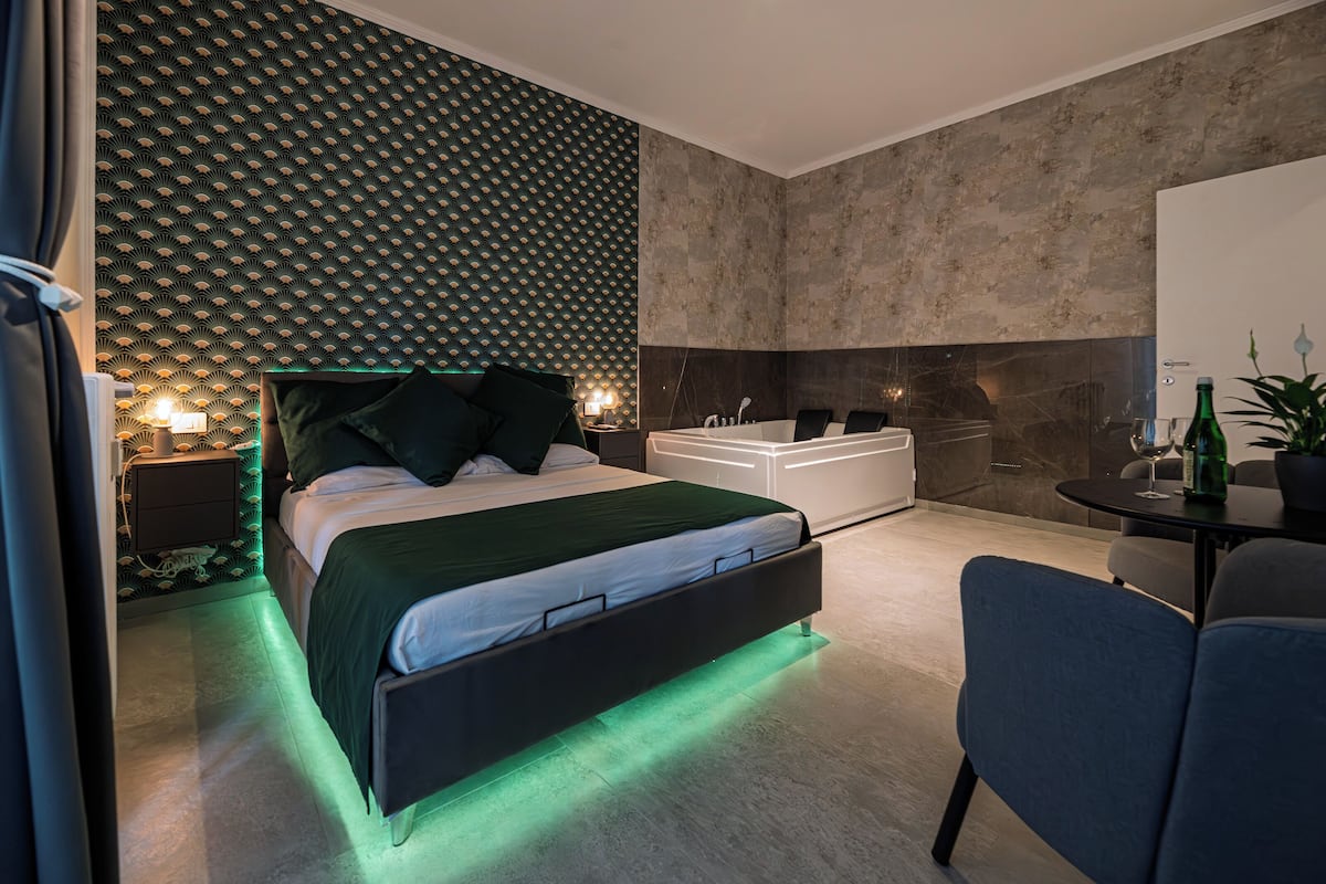 Quarto moderno com cama, mesas de cabeceira, um sofá e uma pequena mesa com uma planta.