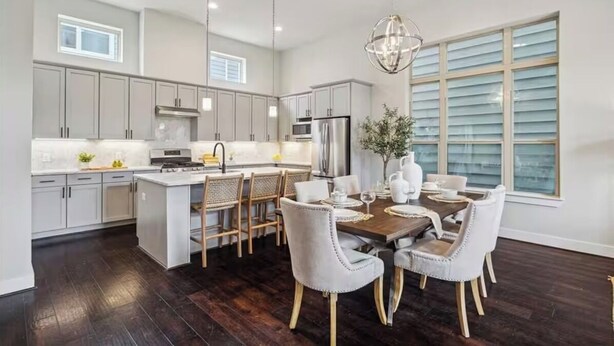 Una cocina moderna con armarios grises, una isla central y una zona de comedor con sillas blancas y una mesa de madera.