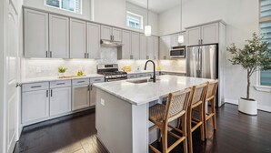 Una cocina moderna con gabinetes grises, una isla central con taburetes de bar, electrodomésticos de acero inoxidable e iluminación colgante.