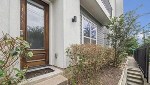 Un edificio residencial con puerta principal de madera, buzón y un pequeño jardín con escalones que conducen a la entrada.