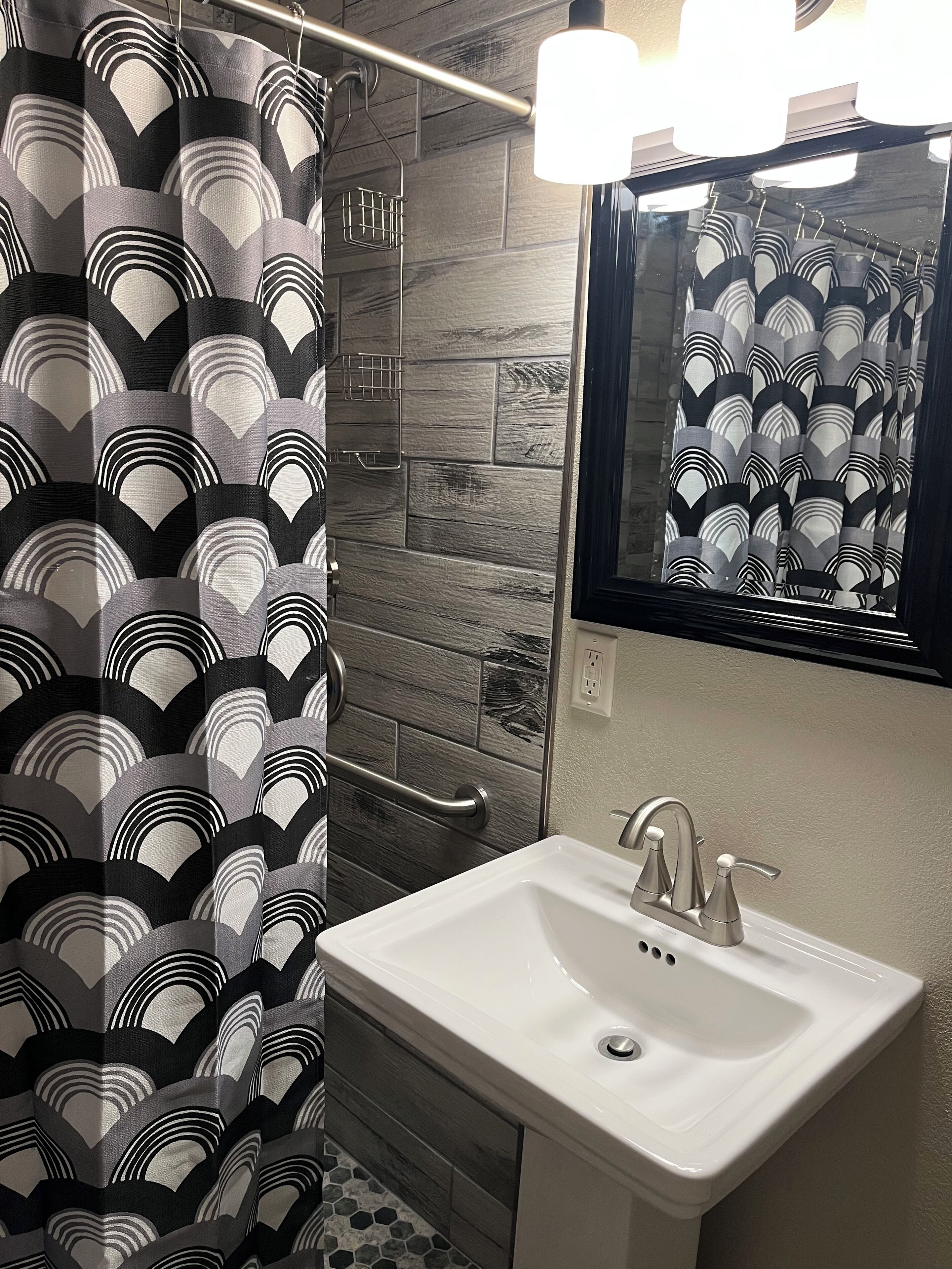 Un baño con cortina de ducha estampada, un lavamanos blanco y un espejo encima.