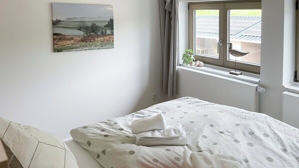 Et soveværelse med en seng, et vindue med gardiner, en radiator og et billede på væggen.