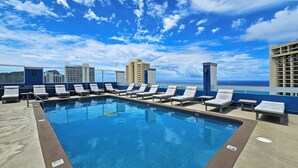 A rooftop pool with lounge chairs and a view of the ocean.