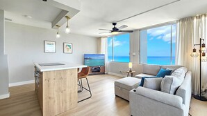 A modern living room with a large window, a ceiling fan, and a flat-screen TV.