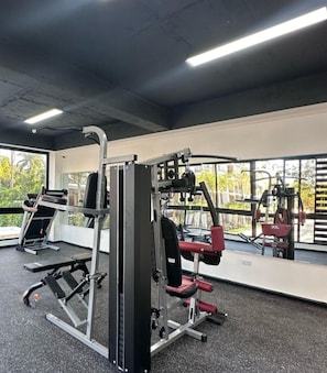Une salle de sport équipée de matériel d’exercice, dotée de grandes fenêtres et offrant une vue sur la verdure.
