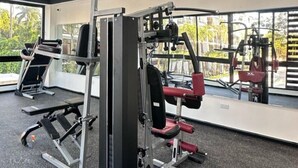 Une salle de sport équipée de divers appareils d’exercice, d’un banc et d’une grande fenêtre donnant sur un espace verdoyant.