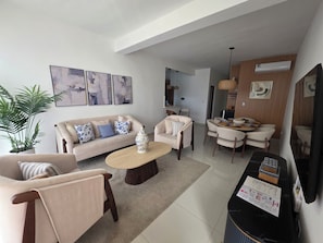Uma sala de estar moderna com um sofá, poltronas, uma mesa de centro e um espaço de jantar com cadeiras e uma mesa.