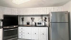 A modern kitchen with white cabinetry, a stainless steel refrigerator, a built-in oven, a microwave, and a decorative chandelier. - IG: @13lacksheep - Vortex (Terrebonne)