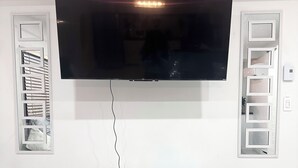 A flat-screen TV mounted on a wall above a silver tufted bench. - IG: @13lacksheep - Vortex (Terrebonne)