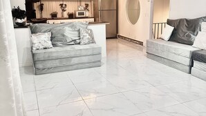 A modern living room with a grey sofa, a dining area with a kitchen in the background, and a large round mirror on the wall. - IG: @13lacksheep - Vortex (Terrebonne)