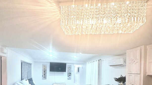 A modern kitchen with a central island, a dining area with a sofa, and a large chandelier. - IG: @13lacksheep - Vortex (Terrebonne)