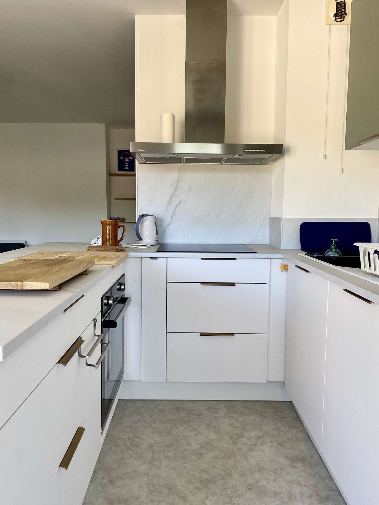 Una cocina moderna con armarios blancos, una campana extractora de acero inoxidable, una tabla de cortar de madera y un hervidor.