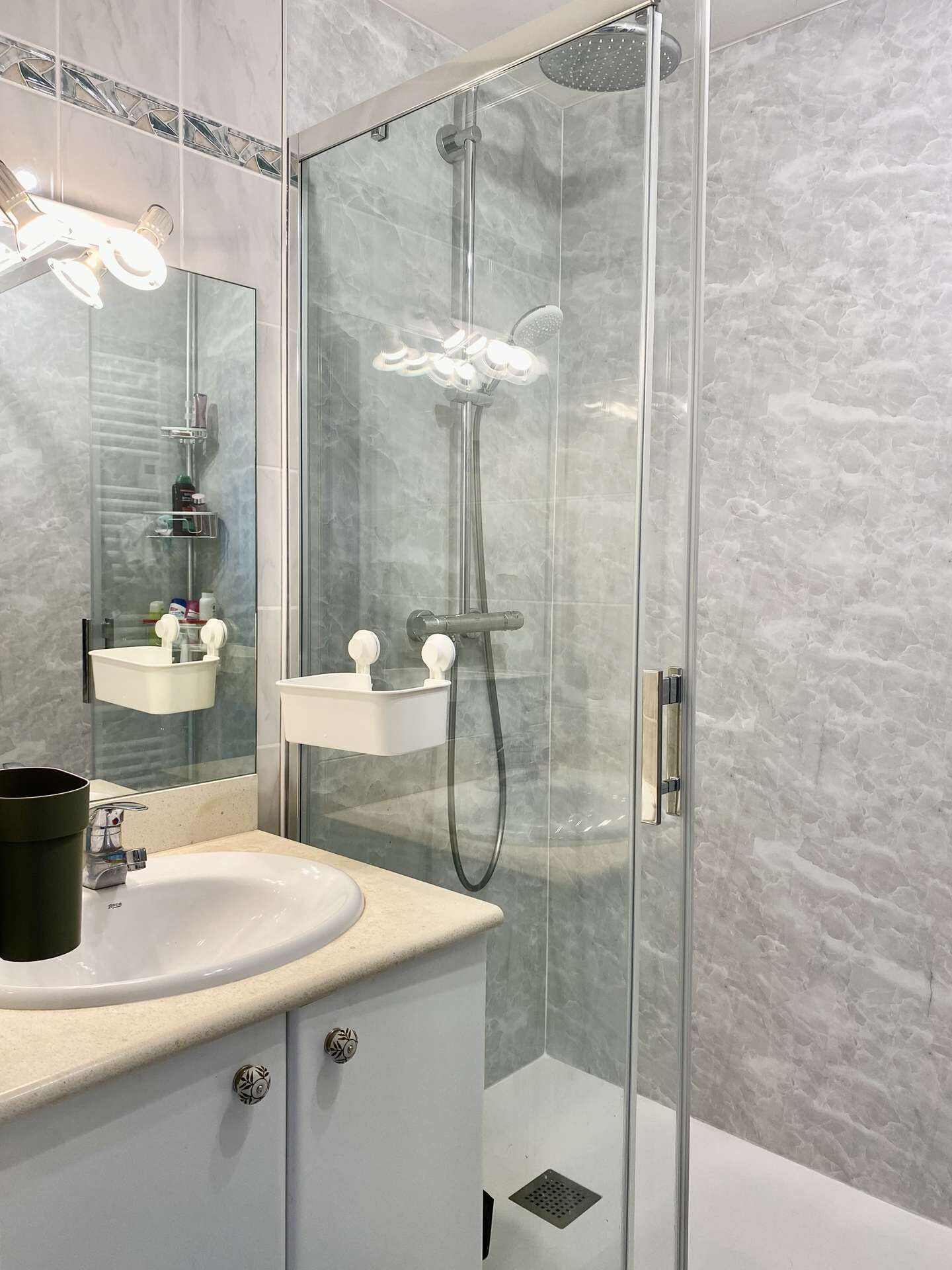 A modern bathroom with a glass-enclosed shower, a white sink, and a mirror with lights.