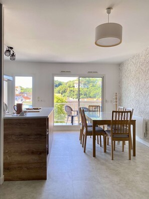 A modern kitchen with a wooden island, a dining area with wooden chairs, and a large sliding glass door leading to a balcony with a view of greenery and buildings. - Renovated two-bedroom flat (55m²), south-facing balcony  et  parking – town centre (ARCACHON)