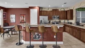 Una cocina moderna con una isla central, taburetes de bar, armarios de madera y un refrigerador.